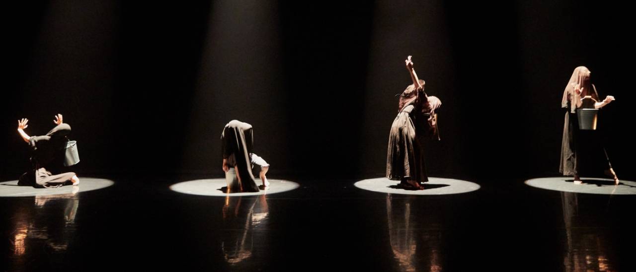 Omerta 4 dancers with buckets each under a spotlight