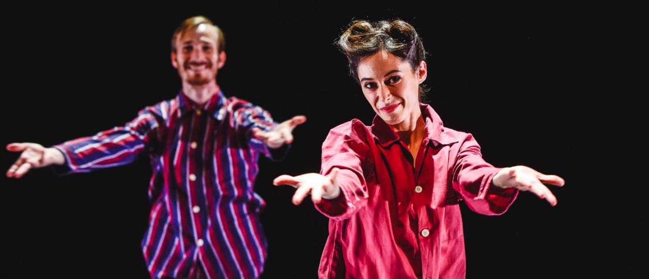 2 dancers, both with their arms stretched out, palms out, smiling to the front. Wearing striped pajamas