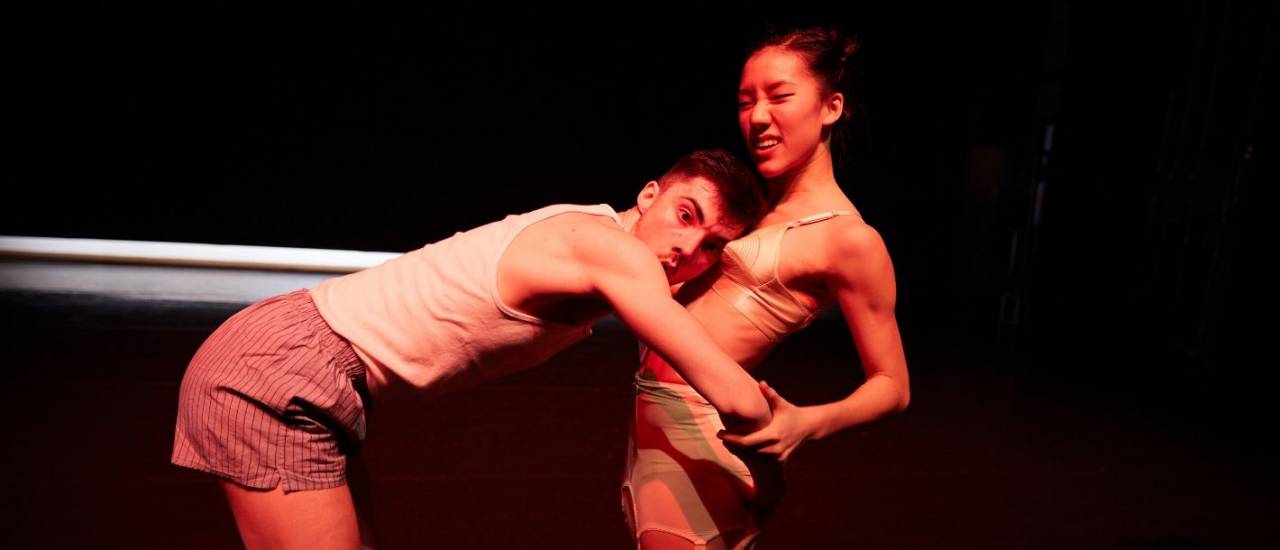 1 male dancer legs spread out, wearing stilettos waving the union jack over his head