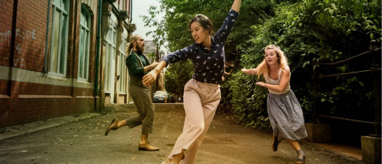 3 dancers, moving in a lane against a brick wall