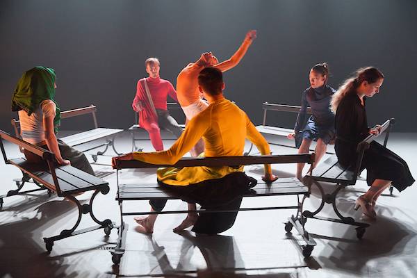 a circle of park benches on wheels and a dancer arching in the centre as they spin around her