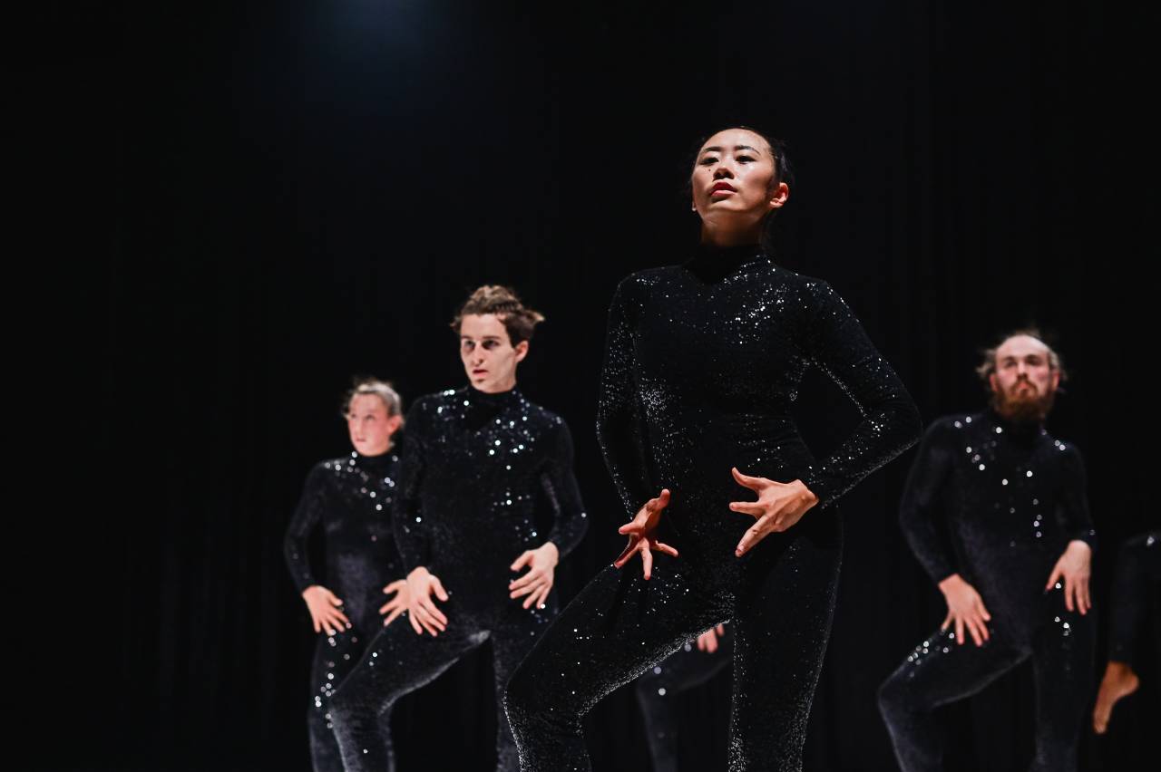 daners in a triangle formation, wearing black sequin catsuits and posing 