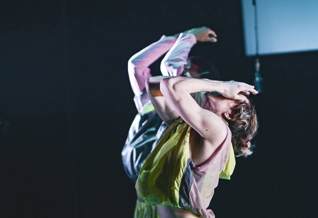 dancer leaning back, hands on face in neon green shirt