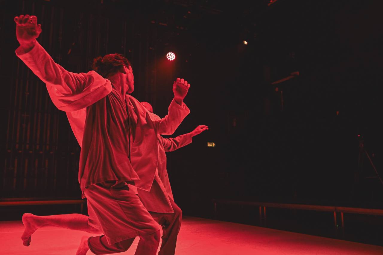 Dancer under red light moves away from the camera, joy in his pose