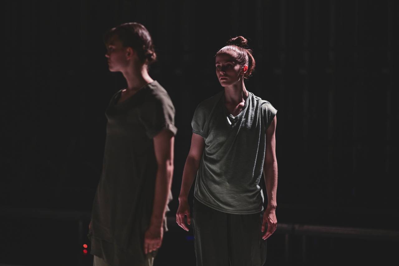 two dancers in earthy costumes looking off into the distance. 