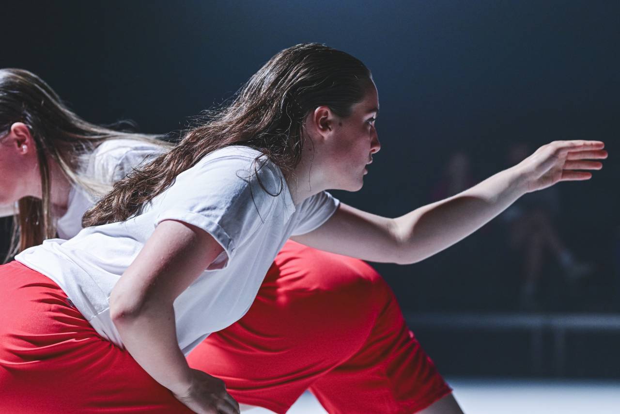 a young dancer leans forward, reaching out as if to touch something, her hair is slicked back