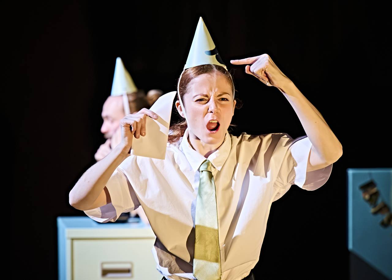 Alys holding a piece of paper and shouting angrily whislt wearing a party hat in Hang in there, Baby by John-William Watson