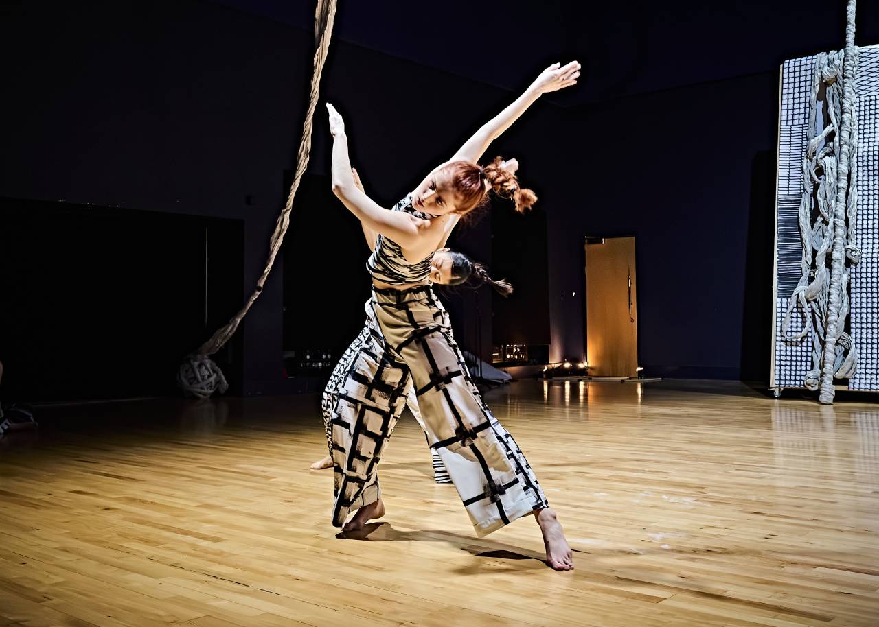 Alys dancing in In Tandem / Infinity Duet by Faye Tan and Cecile Johnson soliz, body and arms moving dynamically away from one another under warm light