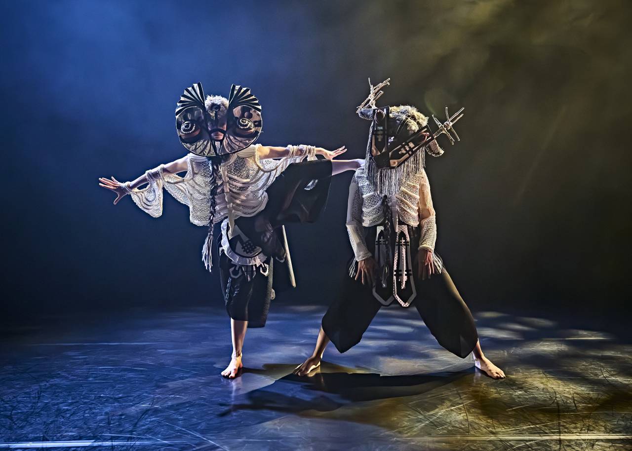 Alys dressed as an owl, her leg raised high, foot resting on the shoulder of another dancer 