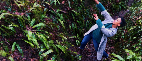 Krystal Lowe dancing in a forest with mud under her feet dressed in a pale green coat