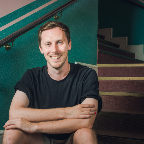 Matthew Robinson sitting on stairs in shorts smiling openly