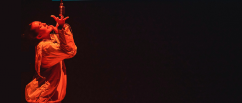 Faye under orange light singing into a vintage microphone wearing colourful street wear