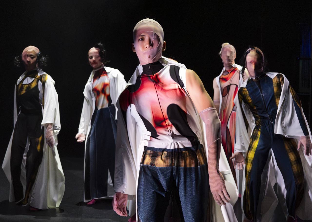 Faye is in tne centre with other dancers around her, she wears a mask of nylon that obscures most of her face and a digital costume printed onto fabric for Skinners by Melanie Lane